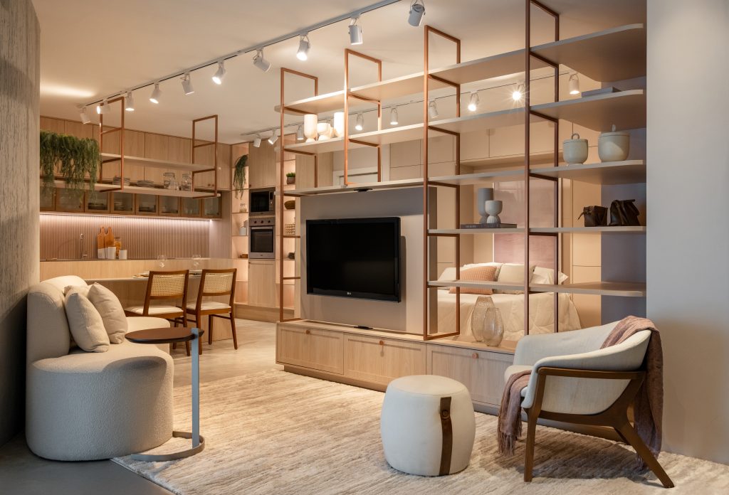 Sala integrada a cozinha e quarto com decoração moderna, iluminação de trilho e estante vazada com TV.