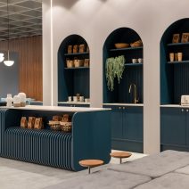 Cafeteria moderna com balcão azul, nichos arqueados, prateleiras decoradas e iluminação pendente.